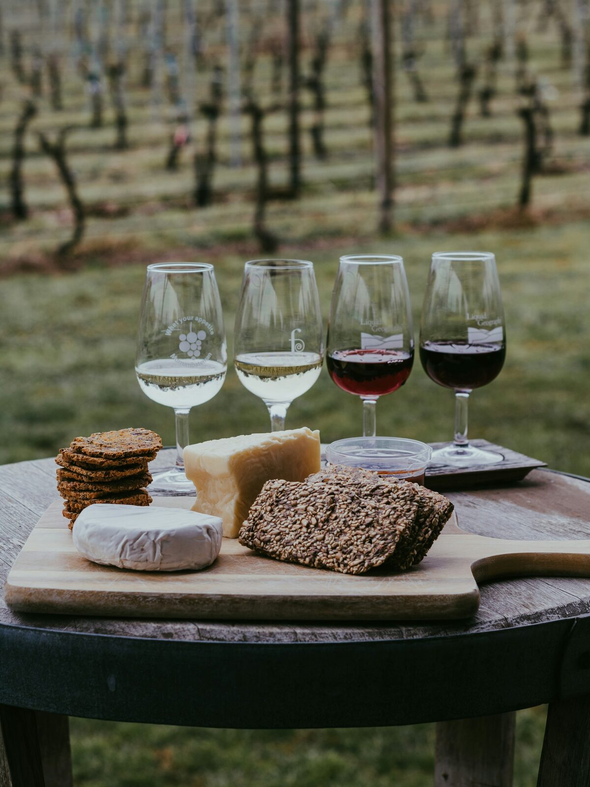 A wine tasting laid out with glasses and a cheese board on a table among the vines.